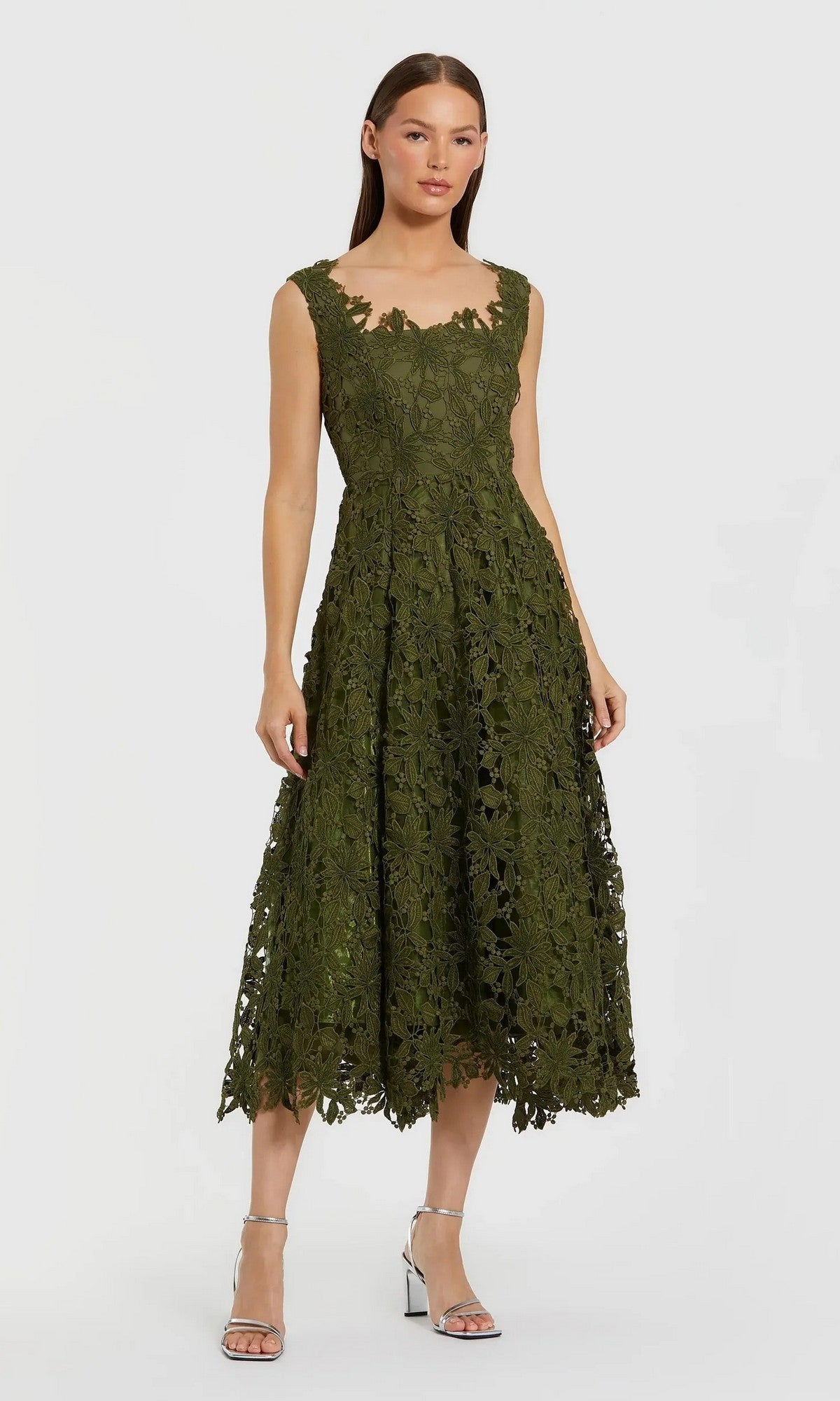 A woman stands wearing the Mac Duggal 69073 Midi Party Dress in Army Green, featuring a sleeveless design with a fitted bodice and flared skirt in a classic A-line midi silhouette, perfectly paired with silver strappy heels.